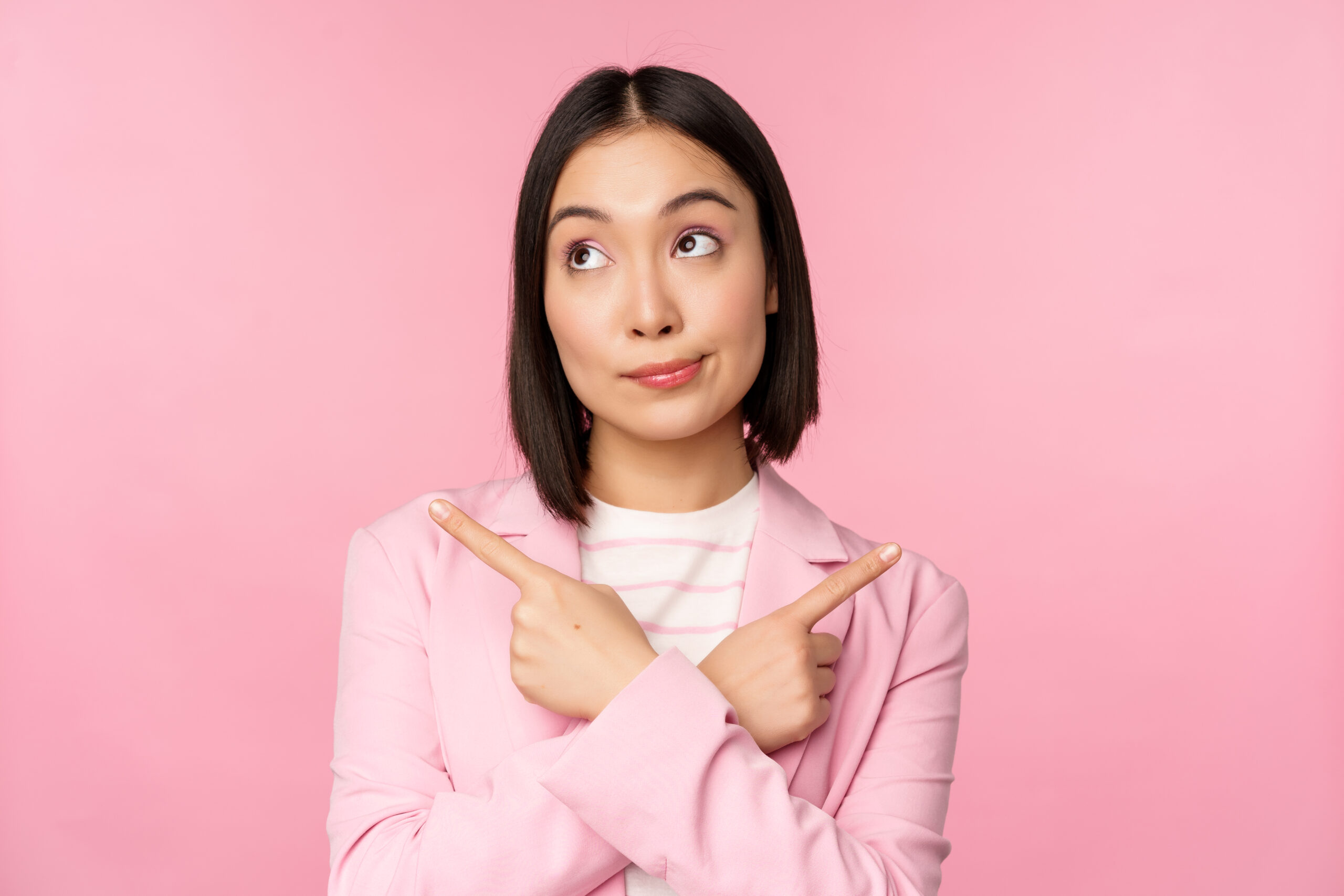decision concept. young asian businesswoman, corporate worker pointing fingers sidways, two directions, showing variants, looking indecisive while choosing, pink background